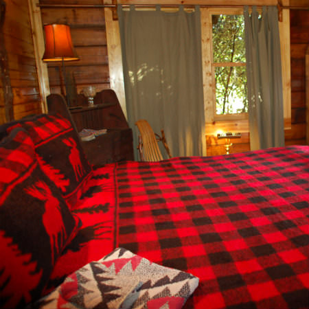 A bright red and black plaid bed lays in the foreground of this rustic guestroom