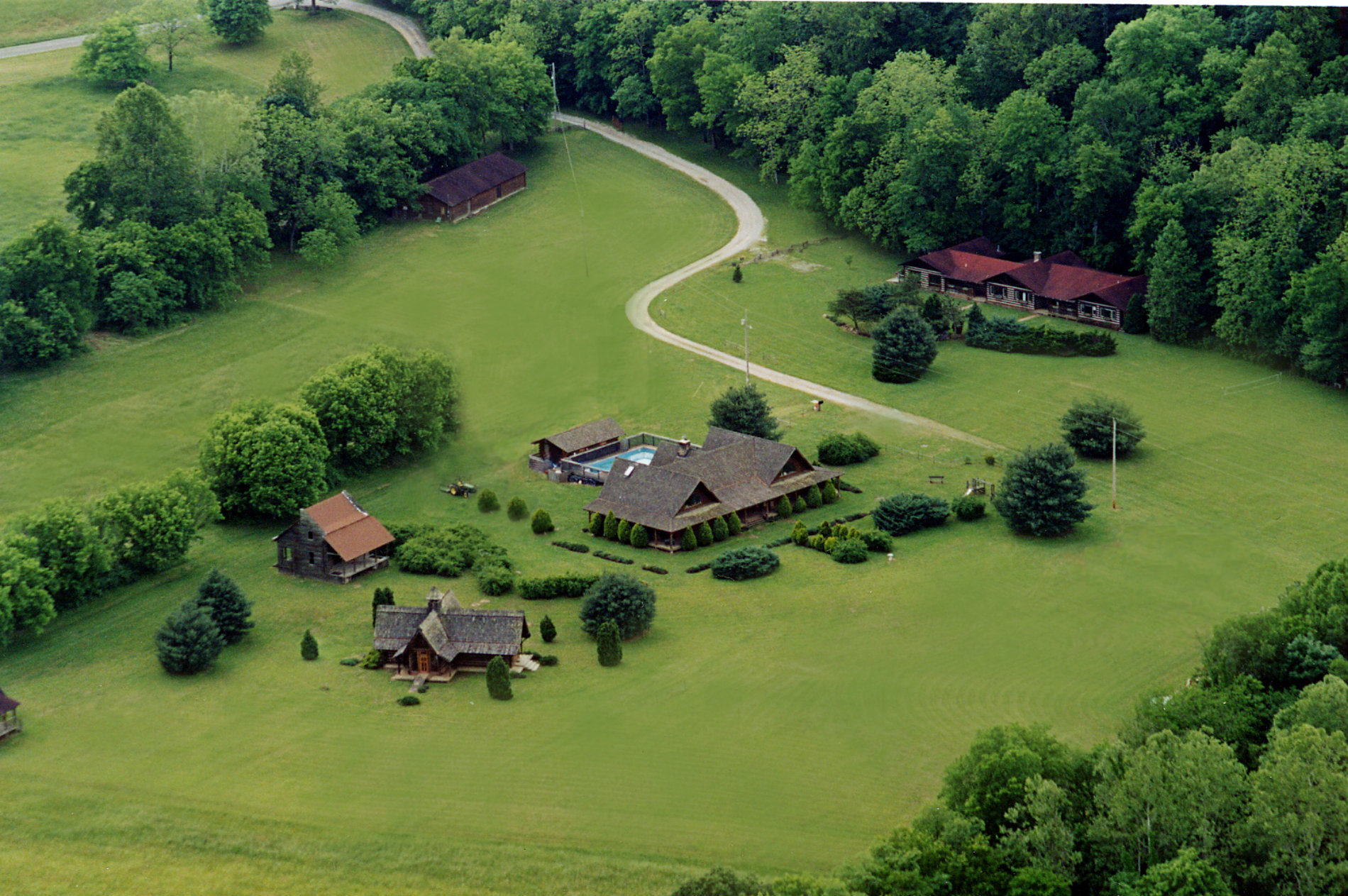 Ariel view of large farm with barn and dirt road and lodge with green trees