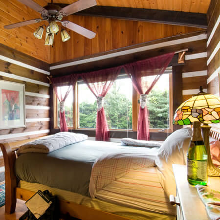 In this cozy guestroom a well-made bed is bathed in sunlight from the open widows with pink curtans