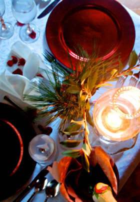 White covered table set for dinner with red dishes and glowing lantern